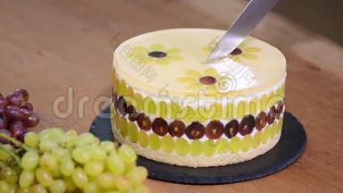 用刀子切慕斯蛋糕和葡萄。 用葡萄装饰的圆慕斯蛋糕。